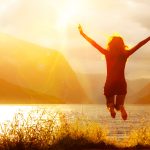 Eine Damen springt freudig in einen Bergsee bei strahlender Sonne