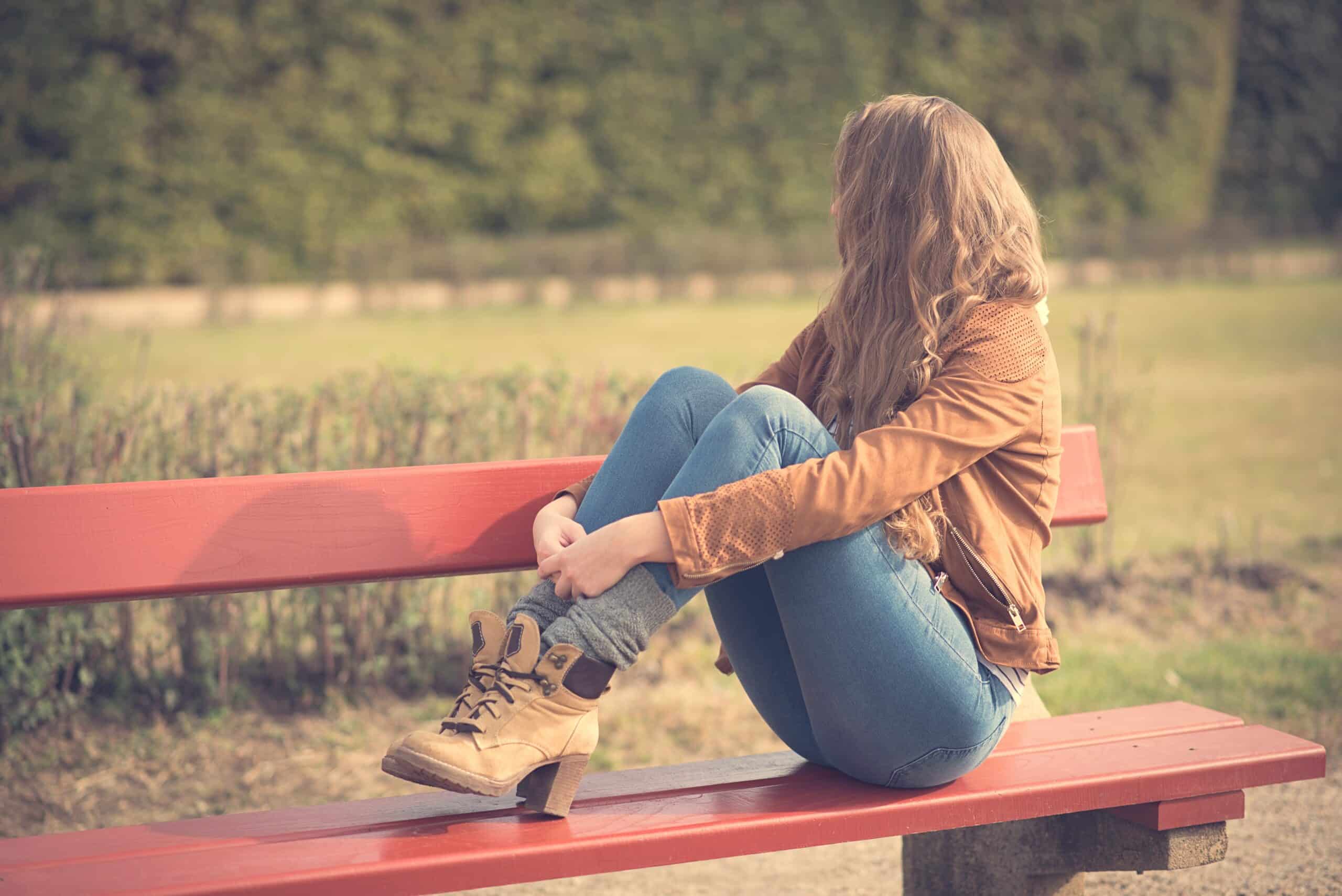 Young woman sitting on the red bench in the sunny park