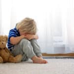 Ein kleiner Junge, der mit seinem Teddy wegen Unfug im Wohnzimmer in der Ecke sitzt. © Tomsickova - stock.adobe.com