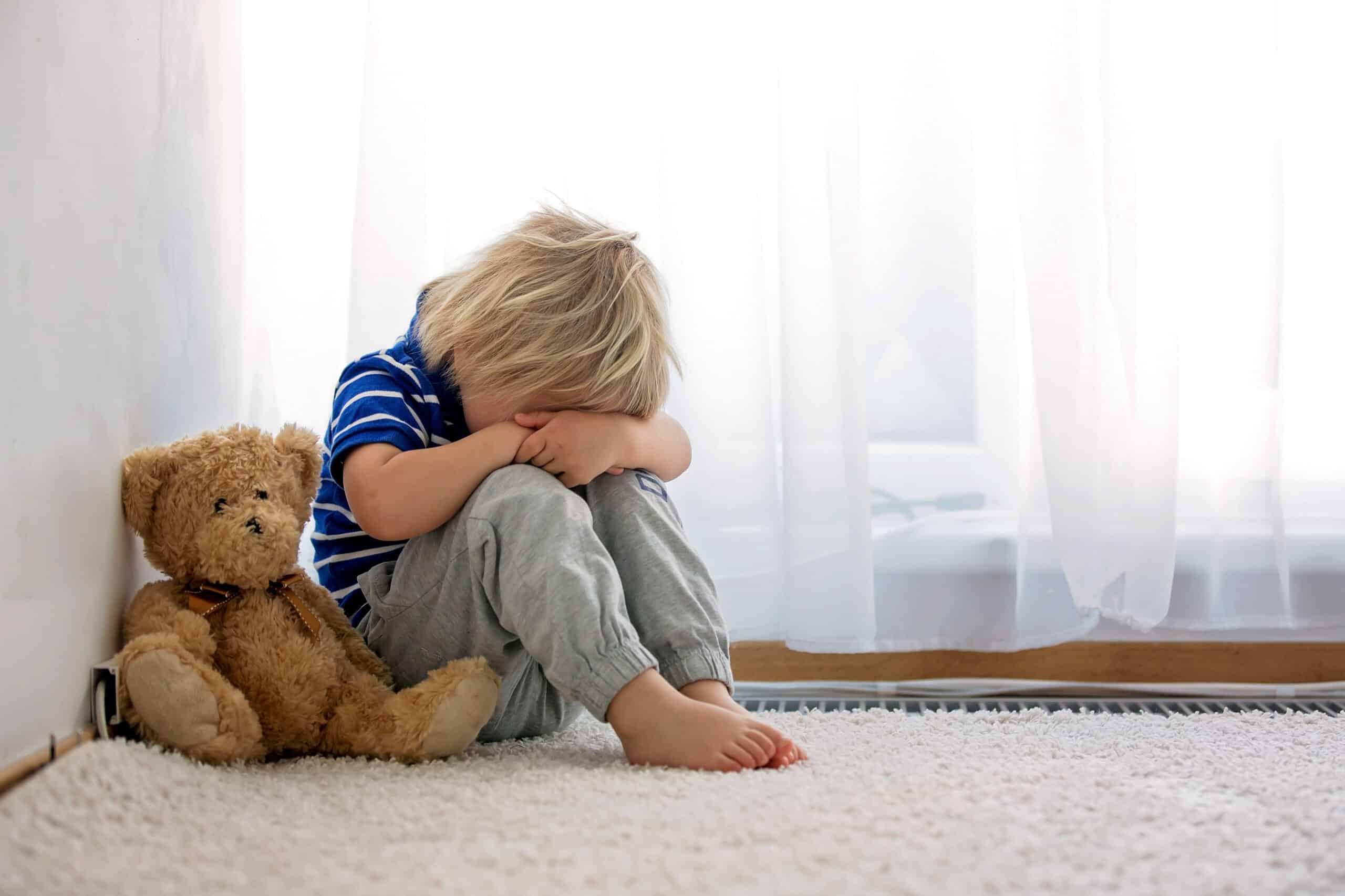 Ein kleiner Junge, der mit seinem Teddy wegen Unfug im Wohnzimmer in der Ecke sitzt. © Tomsickova - stock.adobe.com