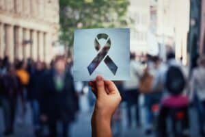 Hand hält Menschen in der Öffentlichkeit ein Blatt Papier mit einer Aidsschleife hin. © 1STunningART - stock.adobe.com